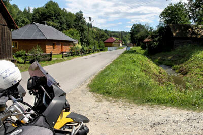 Motorrad parkt auf Seitenstreifen auf Straße, linker Hand zwei Holzhütten