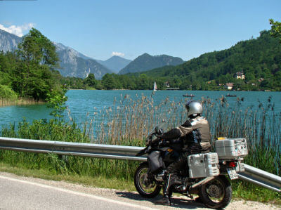 Motorrad steht auf Seitenstreifen mit Leitplanke und blickt über einen Bergsee