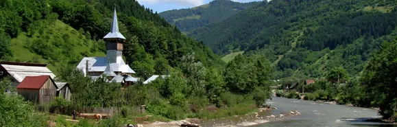 Blick auf im Wald liegende kleine Kirche am Fluss im bewaldeten Wassertal