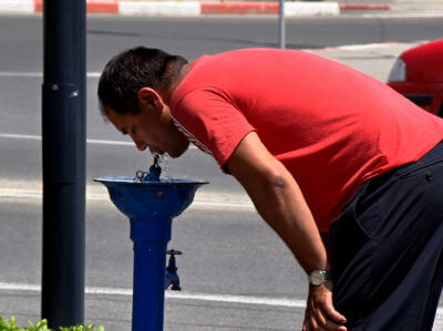 Mann trinkt Wasser aus einem Brunnen an der Straße