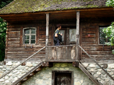 Frau steht vor altem Holzhaus mit Treppen vor der Tür im Freiluftmuseum in Bran