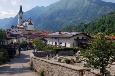 Drežnica ist umgeben von hügeligen Wiesen, die am Bergmassiv des Krn enden. Dorfkulisse mit Kirche und Friedhofsmauer von Drežnica