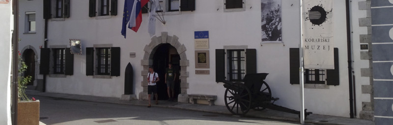 Zwei Leute kommen aus dem Kriegsmuseum in Kobarid. Davor steht eine alte Kanone.