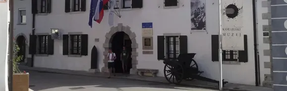 Das Eingangstor zum Kriegsmuseum in Kobarid Zwei Leute kommen aus dem Kriegsmuseum in Kobarid. Davor steht eine alte Kanone.