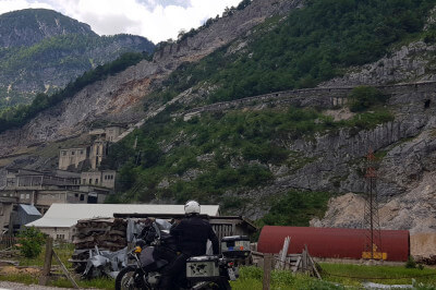 Motorrad vor zerfallenen Gebäuden eines Industriedenkmals der Cave del Predil