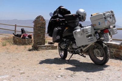 Motorrad steht auf Parkplatz mit Brunnen und Fahrer liegt auf einer Bank in der Sierra de los Filabres