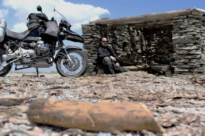 Motorrad steht vor kleiner Steinhütte mit Flachdach indem der Fahrer vor Sonne flüchtet