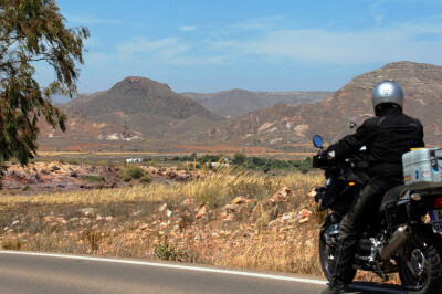 Braune Berge im Hintergrund, steppenartige Landschaft und eine Straße mit einem Motorrad im Vordergrund