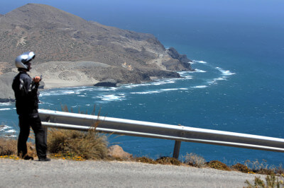 Motorradfahrerin steht an steiler Straße an der Leitplanke zum fotografieren am Cabo de Gata