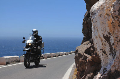 Motorrad fährt auf Küstenstraße direkt am Fels vorbei zum Leuchtturm