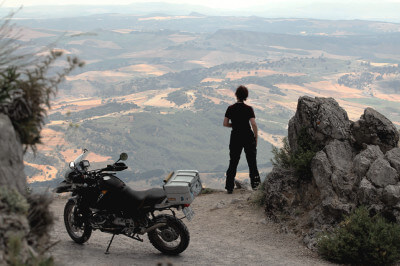 Motorradfahrerin mit Motorrad steht auf Berg mit sagenhaftem Panoramablick auf die Sierra Grazalema