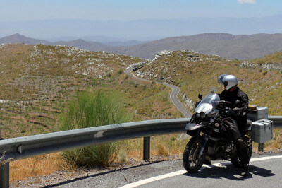 Motorrad steht vor Leitplanke an Bergstrecke und Fahrer genießt den Weitblick ins Tal