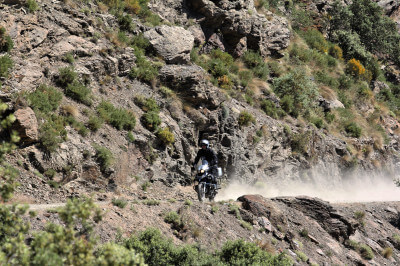 Motorrad fährt mit Staubfahne offroad durch die felsige Landschaft der Sierra Nevada