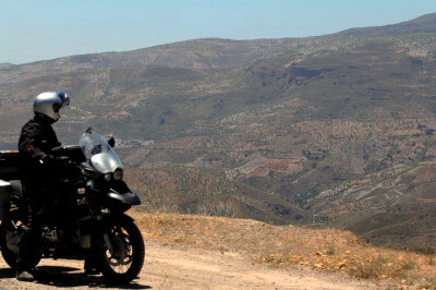 Motorradfahrer steht in der kargen Landschaft der Sierra Nevada