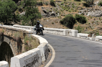 Motorrad fährt über Steinbrücke in der kargen Landschaft der Alpujarras