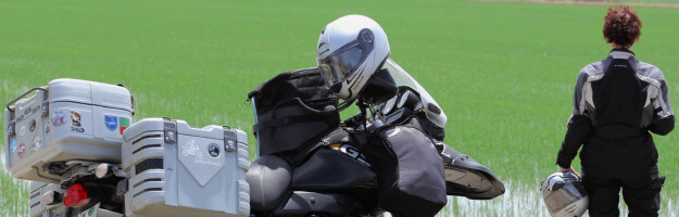 Motorradfahrerin steht vor Reisfeld im Ebro-Delta