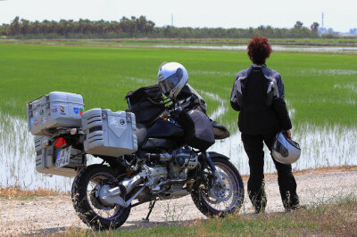 Motorrad und Fahrerin vor Reisfeld im Ebro-Delta