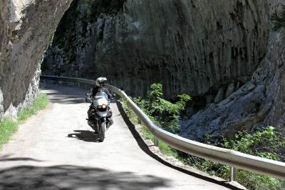 Motorrad fährt unter Felsüberhängen auf schmaler Straße lang am Canyon de Anisclo