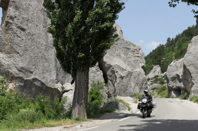 Motorrad fährt zwischen Felsen und Bäumen durch die Drôme: Site du Claps