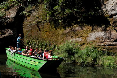 Ein mit Touristen besetztes Boot fährt über einen Fluss in der Böhmischen Schweiz