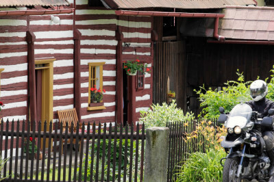 Braun weiß in Streifen bemaltes Blockhaus im Dorf Vesec mit Gartenzaun und Motorrad