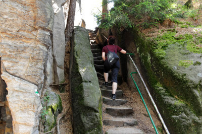 Frau steigt steile Felstreppe mit Handlauf hinauf an den Prachover Felsen