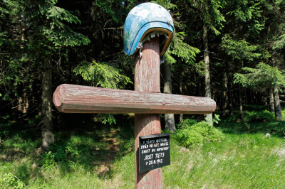 Holzkreuz mit Helm oben drauf neben der Landstraße im Isergebirge