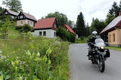 Motorrad fährt auf kleiner Straße durch ein Dorf mit schönen alten Holzhäusern