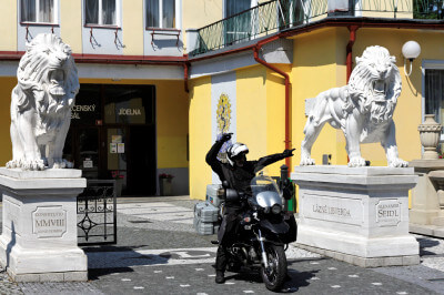 Motorrad steht zwischen zwei weißen Skulturen auf Sockel vor einem Hotel im Isergebirge