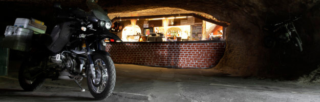 Motorrad steht in einer Höhle vor dem Tresen der Bar in der Bikerhöhle Pekelné Doly