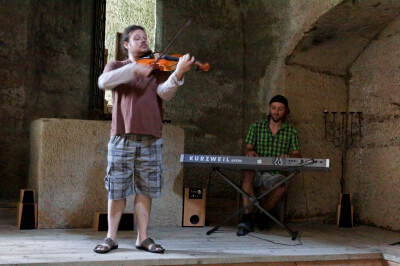 Musiker spielt auf einer Geige in einem Innenraum und wird von einem anderen Instrument begleitet