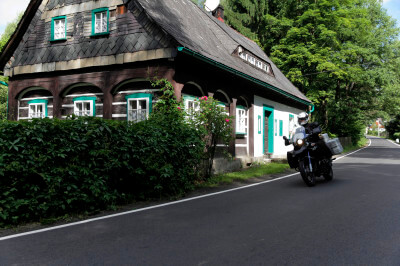 Motorrad fährt an typischem Holzhaus auf Straße vorbei