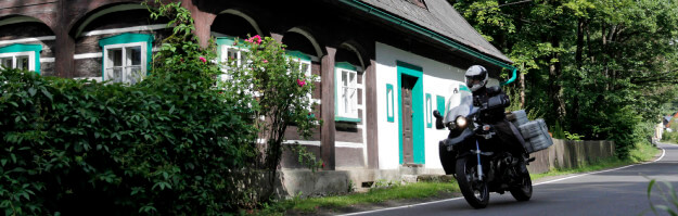 Motorrad fährt an Haus mit grünen Fensterumrandung vorbei in Tschechien