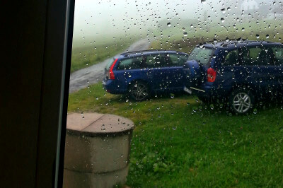 Blick von innen aus dem regennaßen Fenster auf zwei blaue Autos