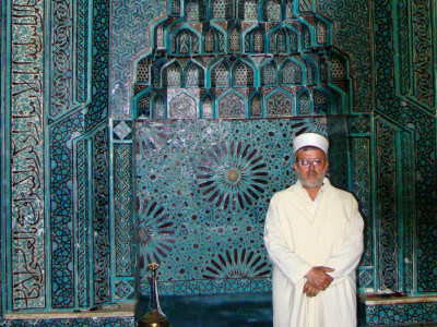 Der Imam der Edrföglu-Moschee vor einer in blau gehaltenen mit Ornamenten verzierten Wand in Beysehir
