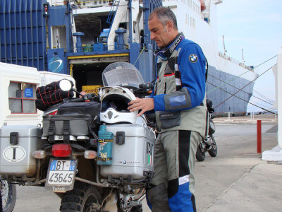 Motorradfahrer steht vor der Fähre beim Check-In im Hafen von Cesme