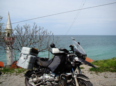 Motorrad steht an Küste im Hintergrund ein Minarett