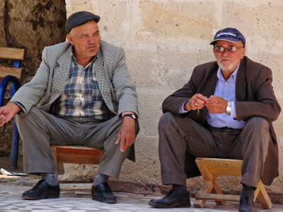 Zwei Männer sitzen beim Gespräch auf kleinen Holzhockern in Mustafapasa